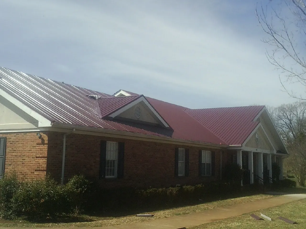 Red metal roof with gabled entries on a long brick building, from a Hail Damage Roof Repair job in Olathe