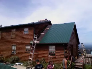 Green metal roof going on a two story log home with ladders set in Olathe