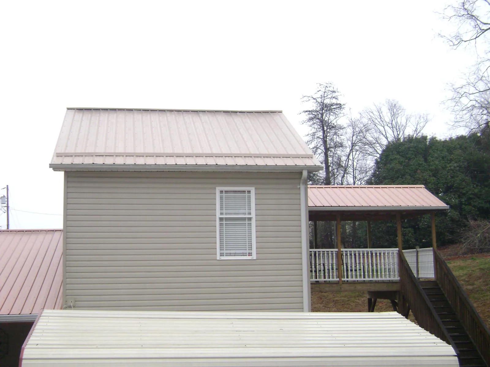 Tan metal roofs on a two story addition and attached porch, from a Roof Replacement job in Olathe